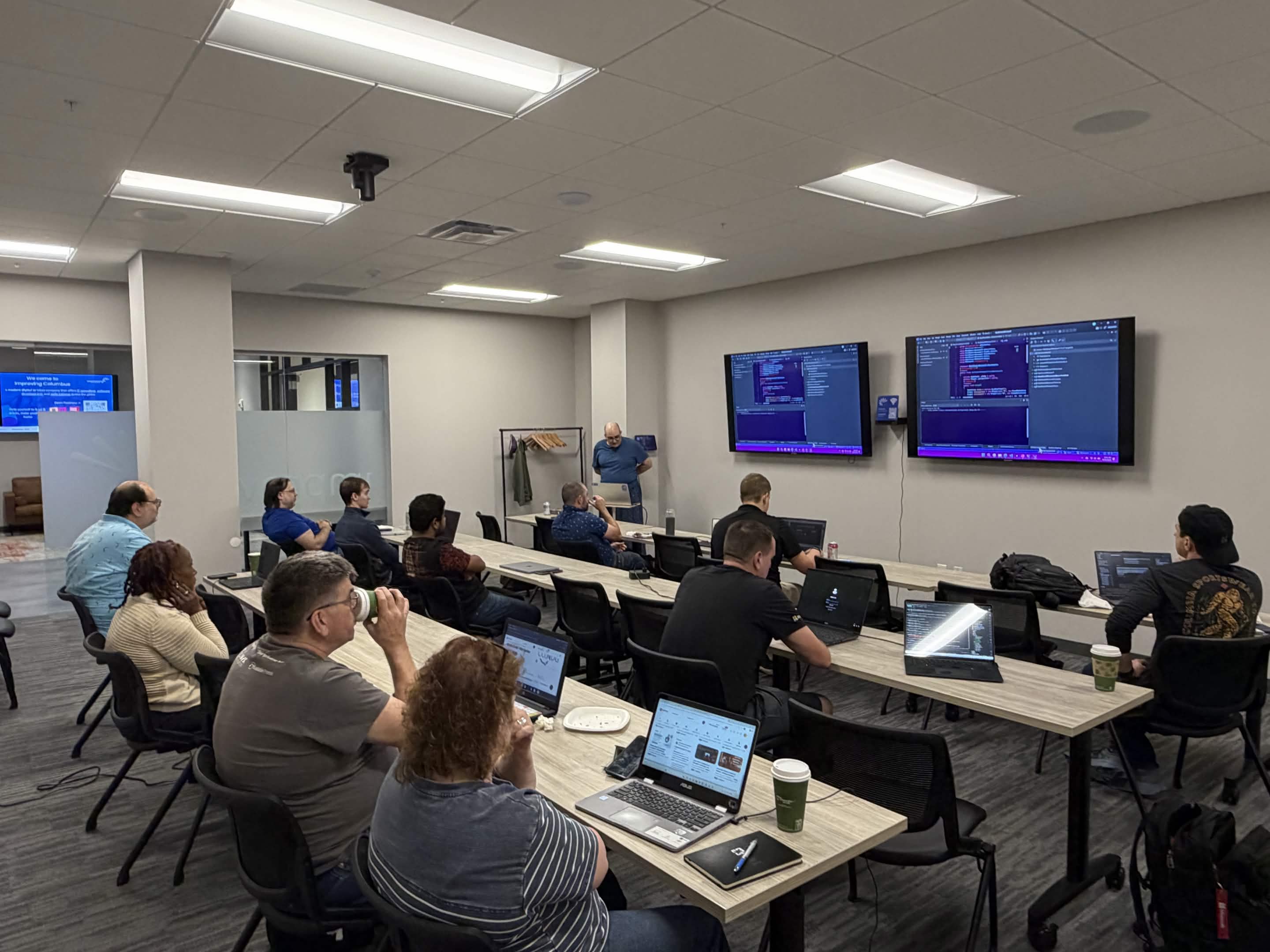 Picture from event showing several people around tables listening to a presentation